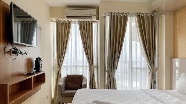 Een hotelkamer met een bed, een stoel, een aan de muur bevestigde televisie en een raam met gordijnen.