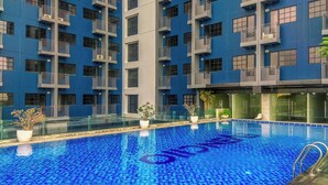 A swimming pool with a blue mosaic tile floor, surrounded by a high-rise building with balconies. - Modern Look And Comfortable Studio Evenciio Margonda Apartment (Depok)