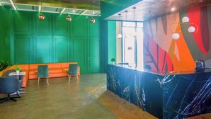 A reception area with a green wall, a marble counter, and a seating area with orange sofas and chairs. - Modern Look And Comfortable Studio Evenciio Margonda Apartment (Depok)