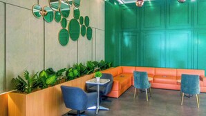 A modern lobby with a green accent wall, a seating area with orange and blue chairs, and a reception desk. - Modern Look And Comfortable Studio Evenciio Margonda Apartment (Depok)