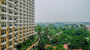 A high-rise building with multiple balconies, surrounded by lush greenery and other residential buildings in the background. - Cozy Living Studio Apartment At Margonda Residence 1 (Depok)
