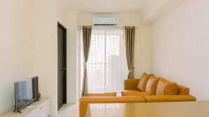 A modern living room with a flat-screen TV on a wooden cabinet, a beige sofa with cushions, and a glass coffee table. - Modern Look And Homey 2Br At Great Western Resort Apartment (Tangerang)