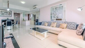 A modern living room with a sofa, coffee table, and a dining area with chairs. - Spacious 3Br At Kemang Village Apartment (Jakarta)