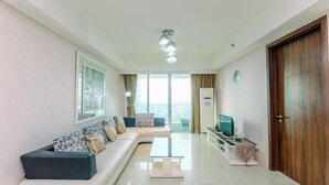 A modern living room with a sofa, a coffee table, a TV, and a door. - Spacious 3Br At Kemang Village Apartment (Jakarta)