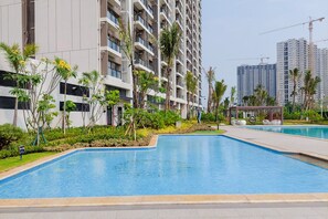 Um edifício residencial moderno com piscina, vegetação exuberante e céu claro.