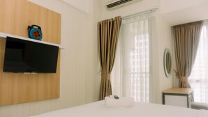 A hotel room with a bed, a flat-screen TV mounted on the wall, a small table, and a chair. - Simply Look And Homey Studio Apartment At M-Town Residence (Gading Serpong)