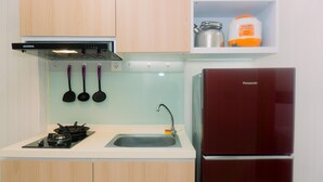 A kitchen with wooden cabinets, a gas stove, a sink, and a red refrigerator. - Simply Look And Homey Studio Apartment At M-Town Residence (Gading Serpong)