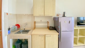 Cocina compacta con armarios de madera, un lavamanos, encimera, refrigerador y una estantería pequeña con una tetera.