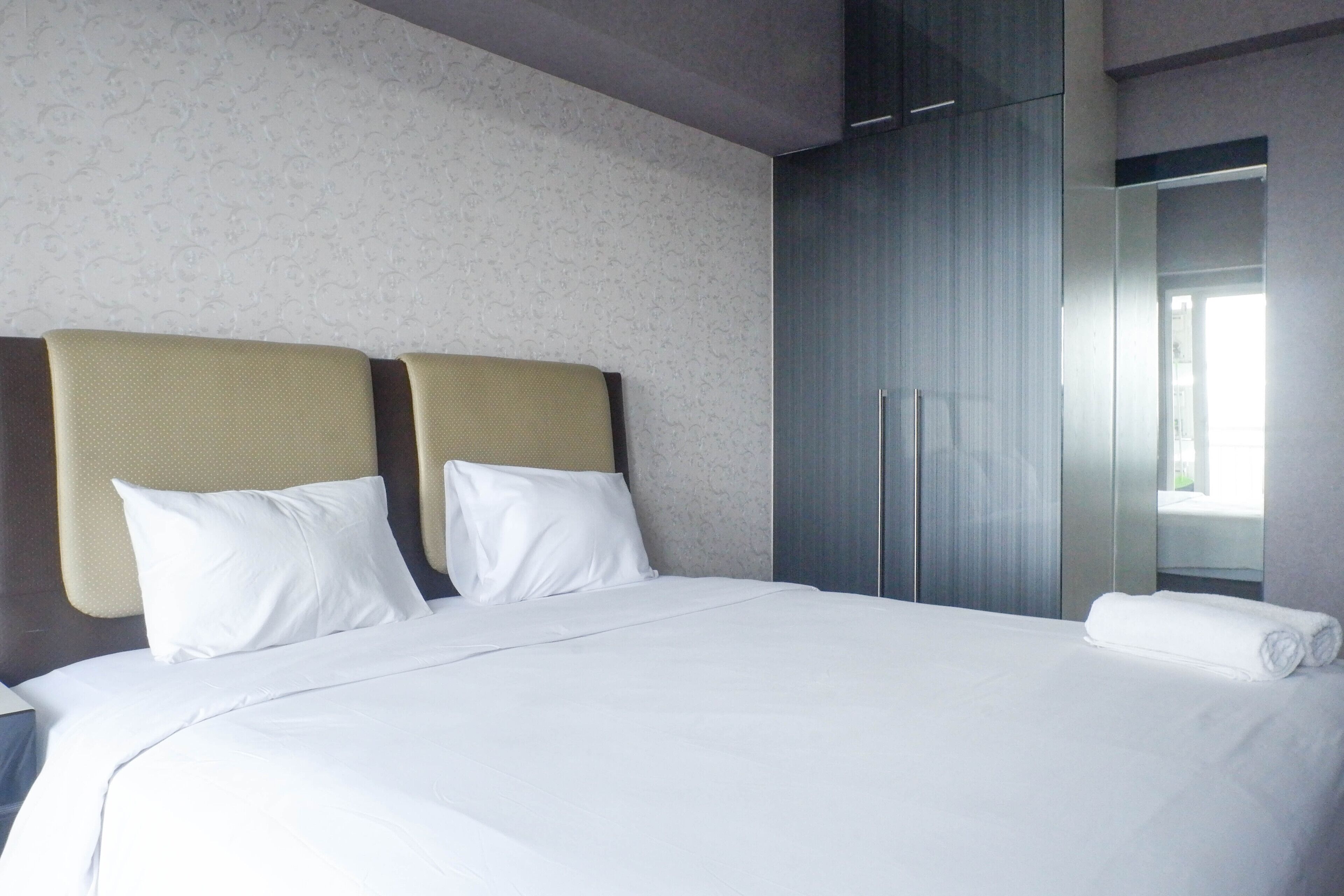 A hotel room with a large bed, two pillows, a neatly made bed, a wardrobe, and a bathroom visible through a glass door.
