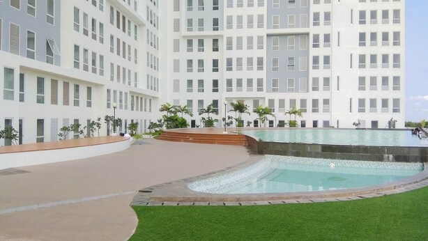 A modern hotel with a large pool area, surrounded by a well-maintained lawn and palm trees. - Cozy Stay And Tranquil Studio Patraland Urbano Apartment (Bekasi)