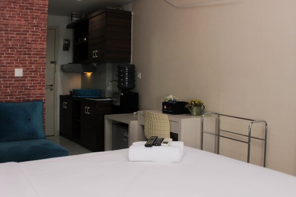 Relax in a compact room with a neatly made bed, desk area, and kitchenette, perfect for working or dining.
