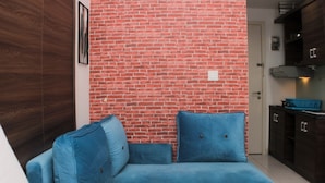 A room with a blue sofa against a brick wall, a wooden cabinet, and a door leading to a kitchen area. - Cozy Stay And Tranquil Studio Patraland Urbano Apartment (Bekasi)