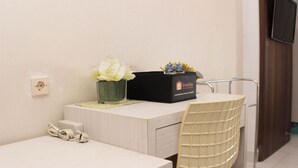 A hotel room with a desk, a chair, a vase with flowers, a black box with the brand name, and a TV mounted on the wall. - Cozy Stay And Tranquil Studio Patraland Urbano Apartment (Bekasi)