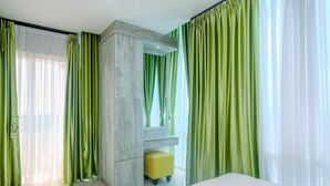 Una habitación de hotel moderna con una cama grande, un armario de madera y cortinas verdes.