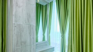 Un baño moderno con tocador de mármol, cortinas verdes y un banco amarillo.