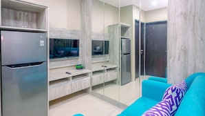 Una sala de estar moderna con televisor empotrado, refrigerador y un sofá color turquesa con cojines estampados.
