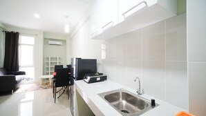 A modern kitchen with a stainless steel sink, a flat-screen TV, and a dining area with a sofa and chairs. - Best Choice And Cozy Living At 2Br At Bale Hinggil Apartment (Surabaya)