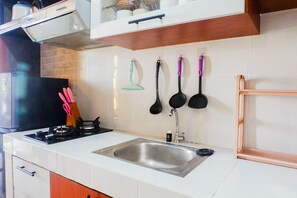 Una cuina amb un rentaplat de thép inoxidable, una cuina de gas i diferents utensilis penjats a la paret.