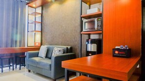 A modern living area with a sofa, a wooden table, and a kitchenette with a microwave and coffee machine. - Modern And Best View 2Br Apartment At Bale Hinggil (Surabaya)