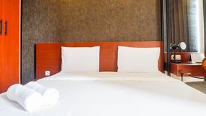 A hotel room with a large bed, wooden headboard, white linens, a nightstand with a lamp, and a calendar. - Modern And Best View 2Br Apartment At Bale Hinggil (Surabaya)