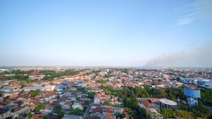 Paisatge urbà amb habitatges compactes, una torre blava destacada i una columna de fum llunyana.