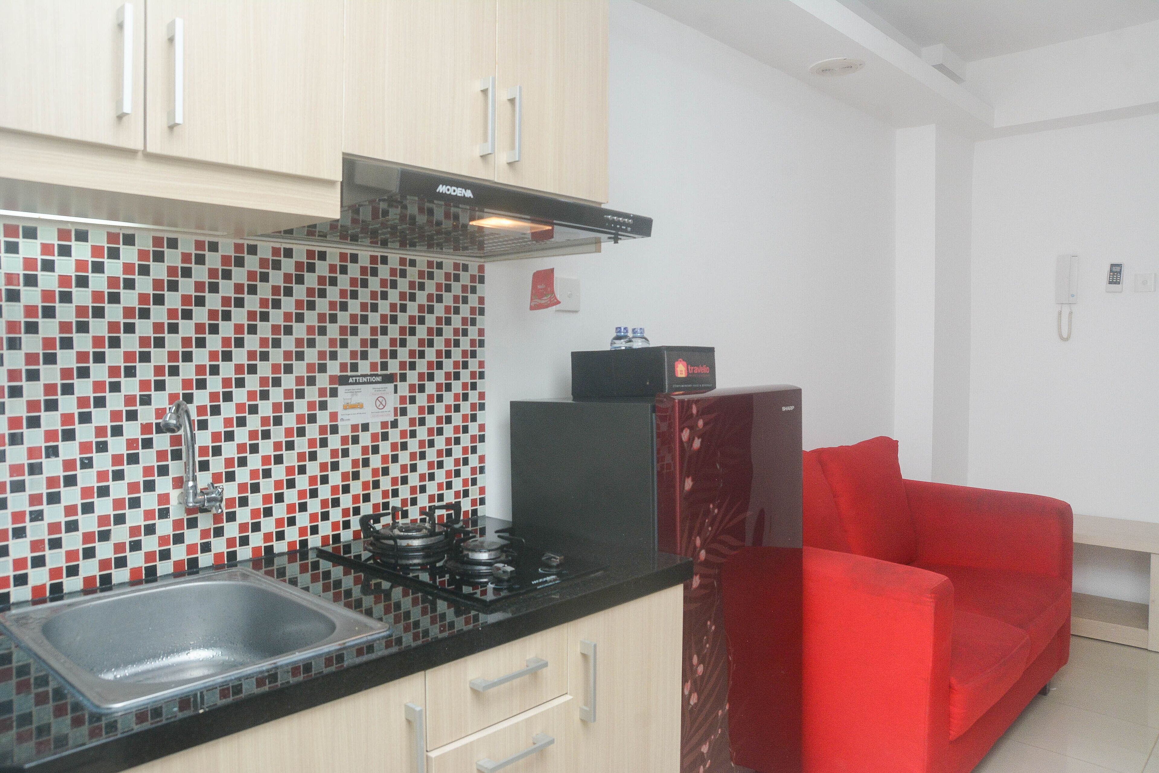 Une cuisine avec un mur recouvert de carreaux, une cuisinière à gaz, un évier et un canapé rouge.