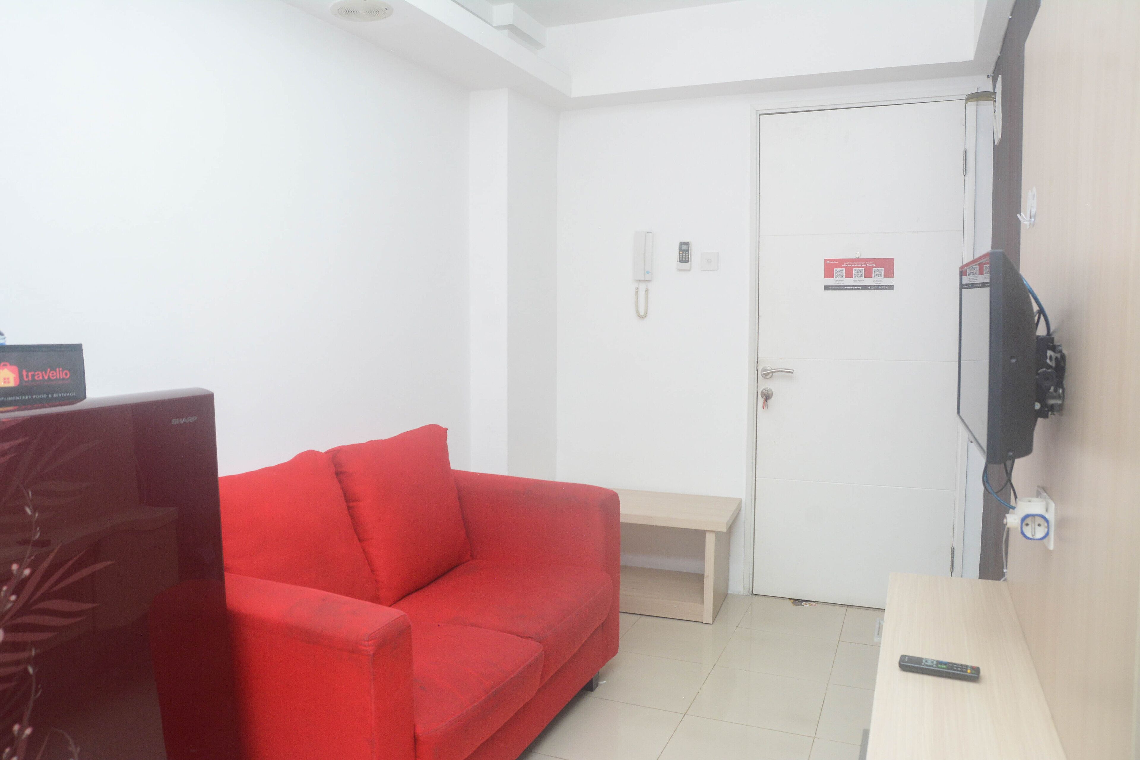 Una stanza con un divano rosso, un tavolino, una TV montata a parete e una porta con il segnale di allarme incendio.
