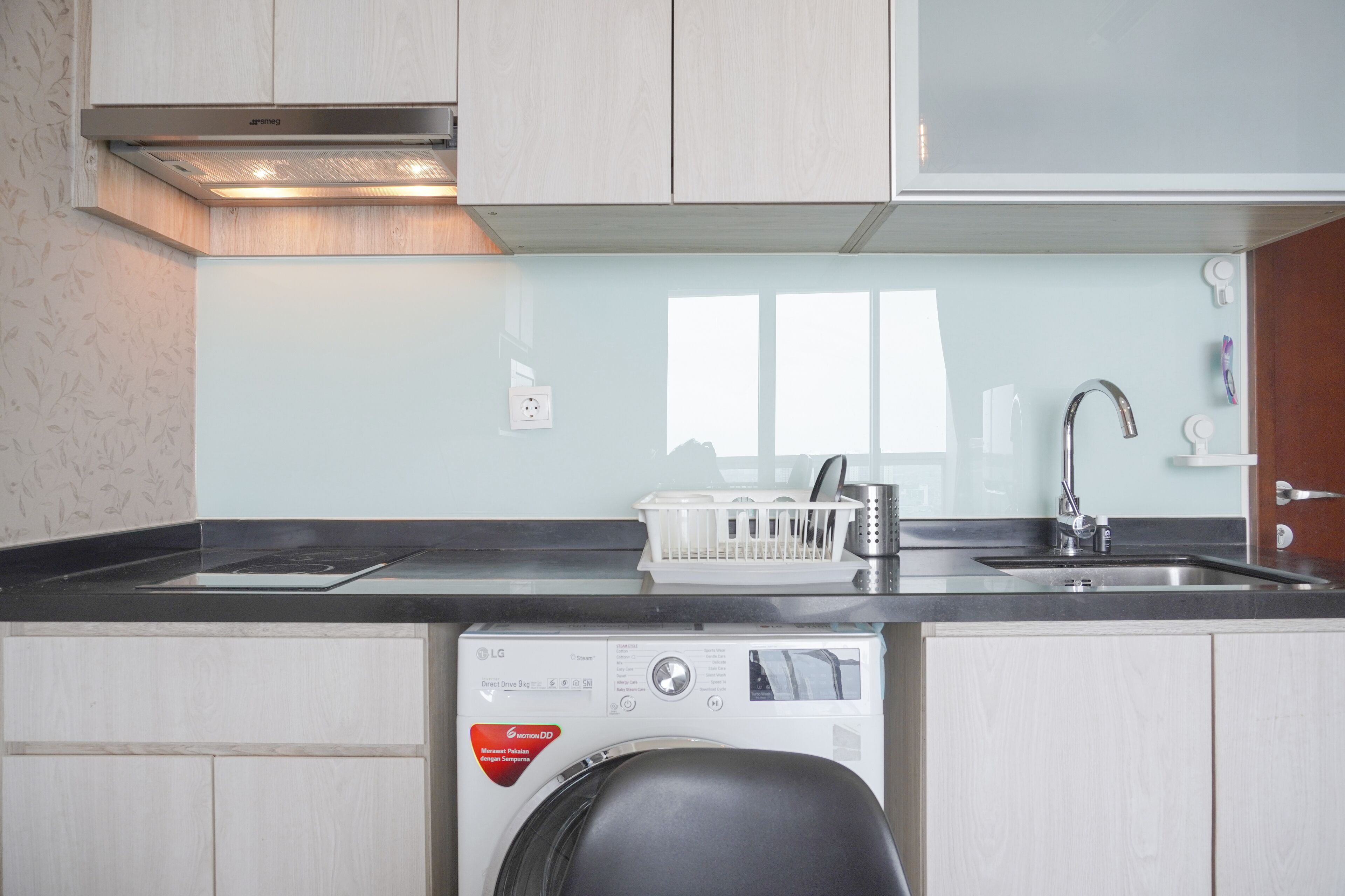 A compact kitchen with a built-in washing machine, a sink, and a window providing natural light.