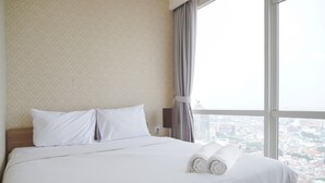 A hotel room with a large bed, two pillows, a neatly folded towel, and a view of a cityscape through a large window. - Modern And Elegant 2Br At Menteng Park Apartment (Jakarta)