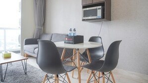 A modern living room with a round table, four black chairs, a grey sofa, a grey curtain, and a microwave above a wooden cabinet. - Modern And Elegant 2Br At Menteng Park Apartment (Jakarta)