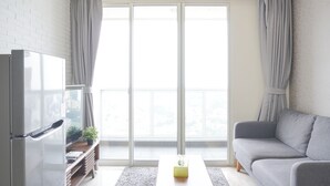 A modern living room with a flat-screen TV, a grey sofa, and a large window with curtains. - Modern And Elegant 2Br At Menteng Park Apartment (Jakarta)