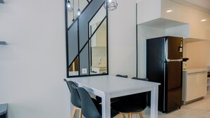A modern kitchen with a white table and black chairs, a black refrigerator, and a built-in oven. - Best Spacious And Homey 3Br At Sky House Bsd Apartment (Pagedangan)
