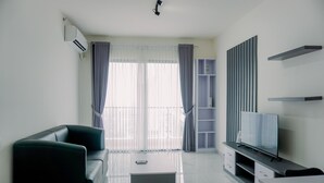 A modern living room with a sofa, a coffee table, a flat-screen TV, and a built-in shelving unit. - Best Spacious And Homey 3Br At Sky House Bsd Apartment (Pagedangan)
