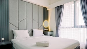 A modern hotel room with a large bed, a nightstand, a wall-mounted light, and a window with curtains. - Best Spacious And Homey 3Br At Sky House Bsd Apartment (Pagedangan)