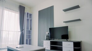 A modern living room with a flat-screen TV, a white desk, and a built-in shelving unit. - Best Spacious And Homey 3Br At Sky House Bsd Apartment (Pagedangan)