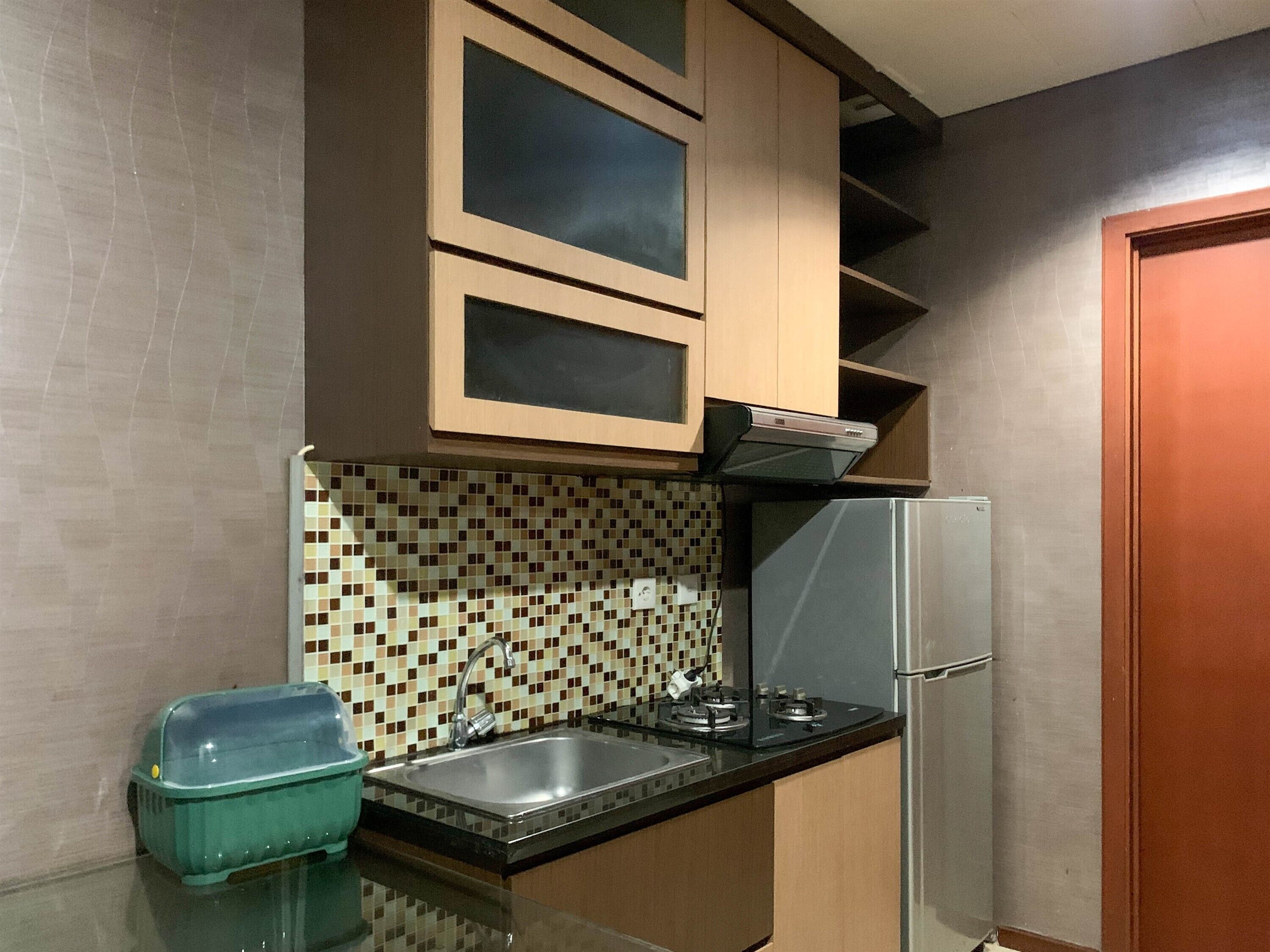A compact kitchen with a tiled backsplash, a stainless steel sink, a gas stove, and a refrigerator.