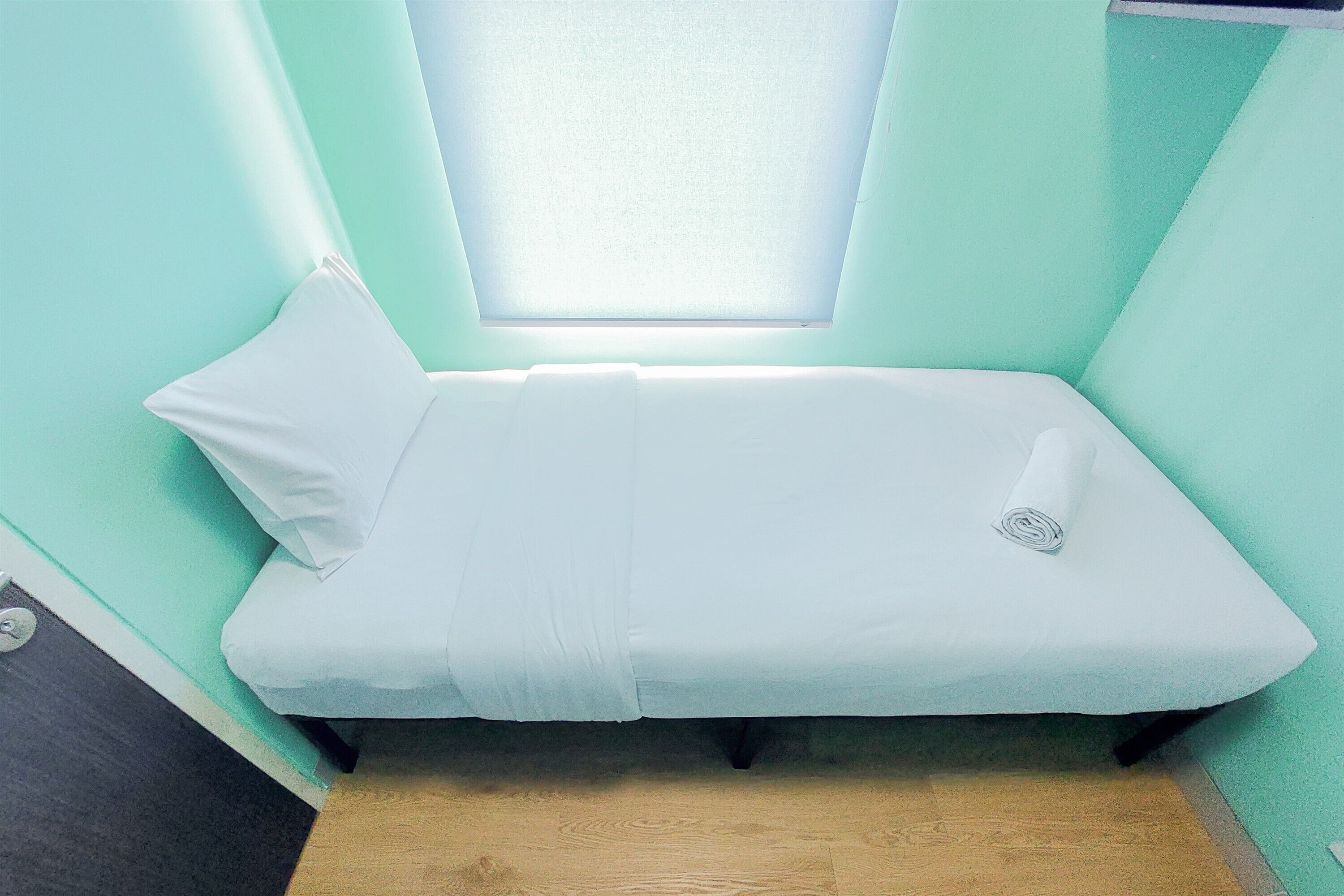 A small, single-bed room with a skylight, a white bedspread, and a rolled towel on the bed.
