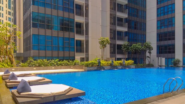 A swimming pool with lounge chairs and a view of modern buildings. - Comfortable 2Br At Apartment Casa Grande Residence (Jakarta)
