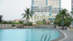 A swimming pool with a curved edge, surrounded by palm trees and a building with a modern design in the background. - Good Location And Cozy Studio Margonda Residence 2 Apartment (Depok)