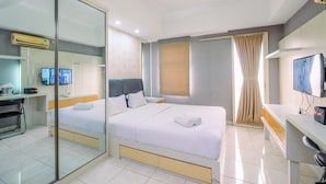 A hotel room with a bed, a desk, a television, and a mirror. - Good Location And Cozy Studio Margonda Residence 2 Apartment (Depok)