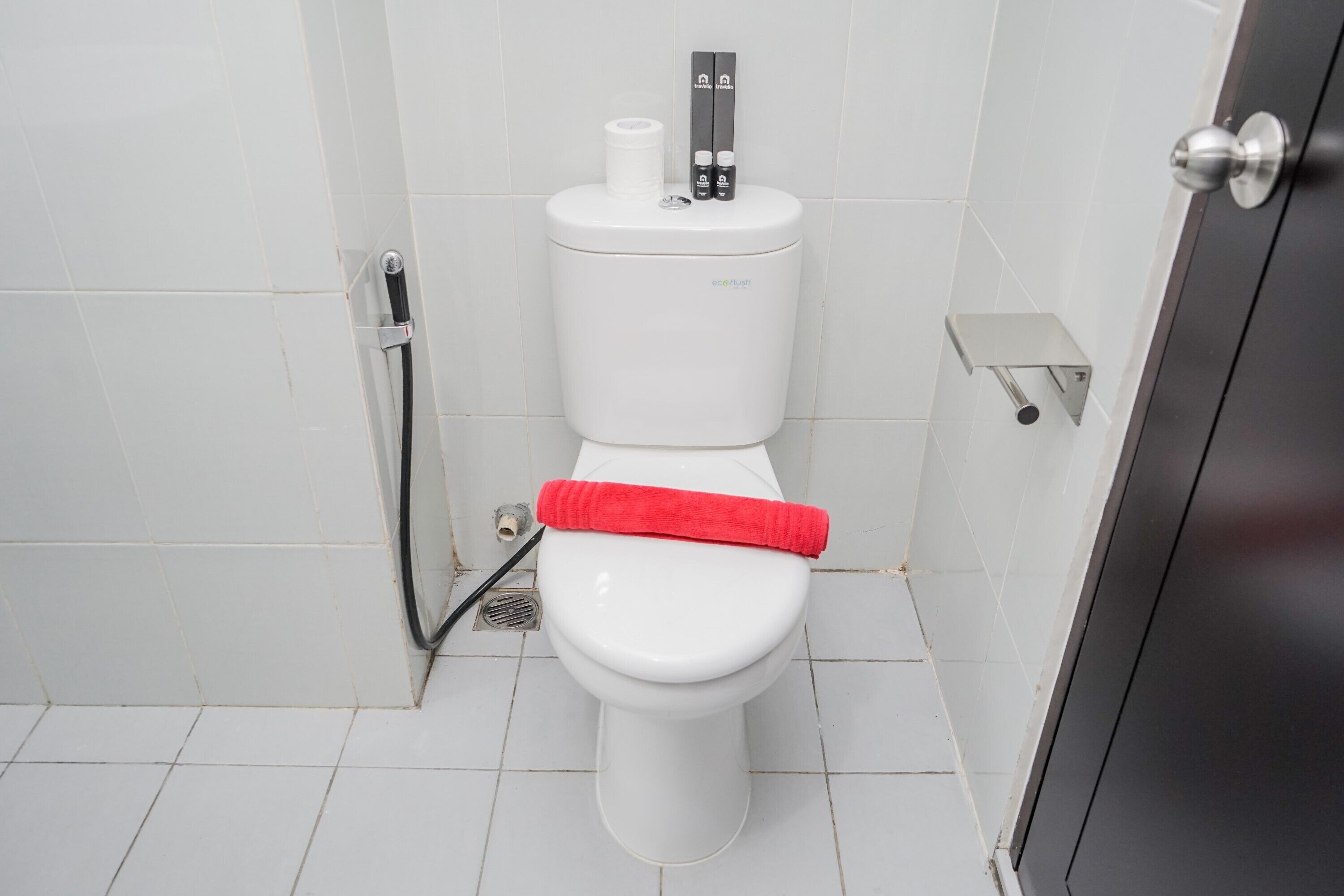 Inodoro blanco con toalla roja, un bidé y un dispensador de papel higiénico.