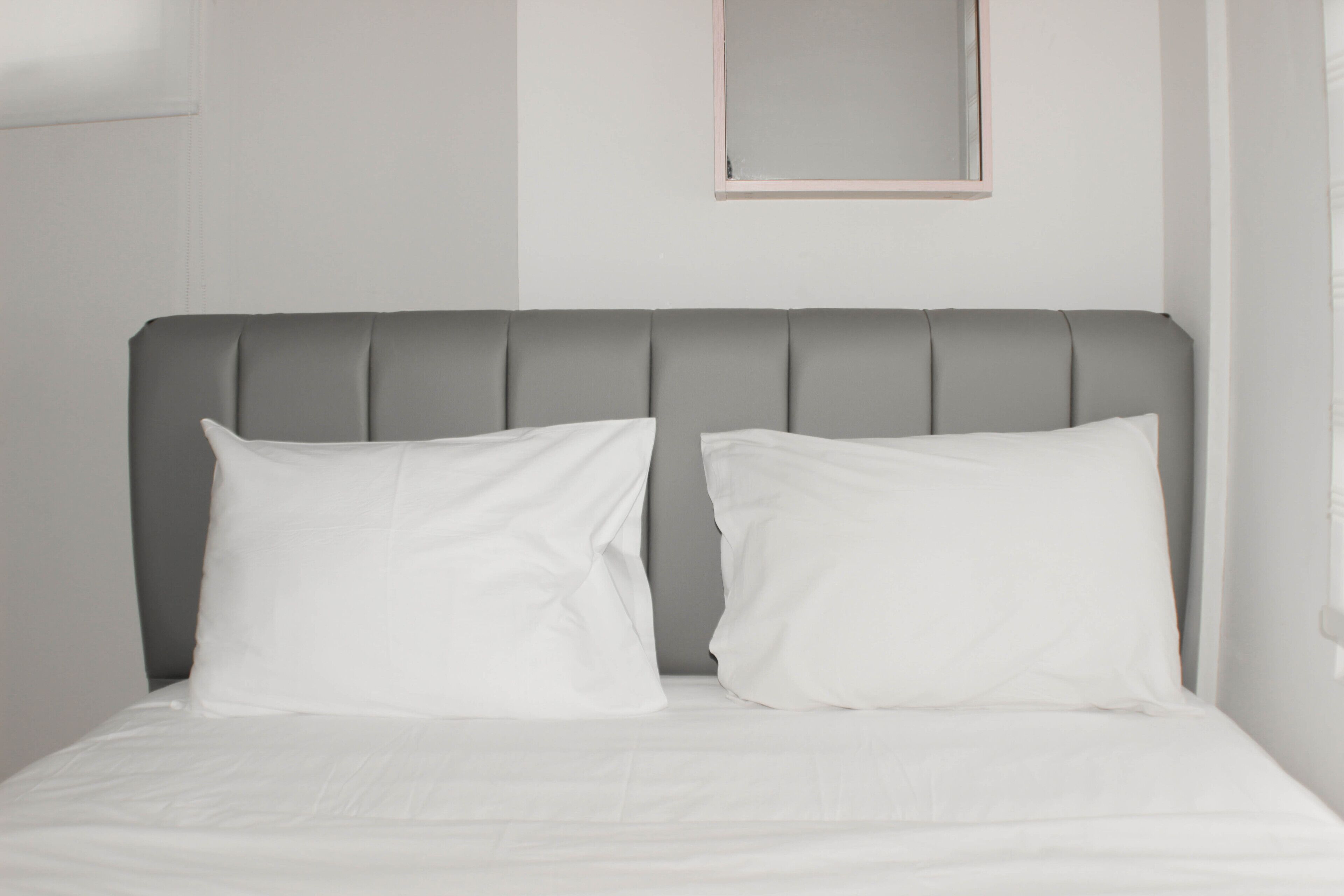 A bed with a grey upholstered headboard and white bedding.