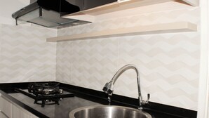 A kitchen with a stainless steel sink, black countertop, and a gas stove. - Comfort Living 3Br At Springlake Summarecon Bekasi Apartment (Bekasi)