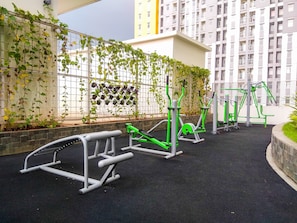 An outdoor gym area with exercise equipment, surrounded by a high wall with climbing plants. - Comfort Living 3Br At Springlake Summarecon Bekasi Apartment (Bekasi)