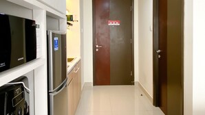A narrow hallway with a Samsung refrigerator, a microwave, and a stove on the left, leading to a door with a fire safety sign. - Comfortable Stay Studio At Pollux Chadstone Apartment (Cikarang)