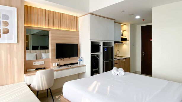 A hotel room with a bed, a desk, a television, a microwave, and a refrigerator. - Comfortable Stay Studio At Pollux Chadstone Apartment (Cikarang)
