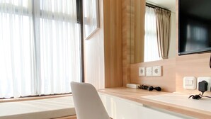 A modern hotel room with a white desk, a chair, a large mirror, and a television mounted on the wall. - Comfortable Stay Studio At Pollux Chadstone Apartment (Cikarang)