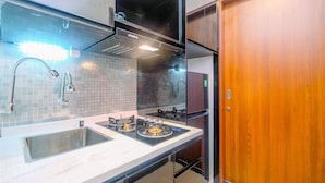 A modern kitchen with a stainless steel sink, a gas stove, and a black range hood. - Spacious 1Br At Grand Kamala Lagoon Apartment (Bekasi)