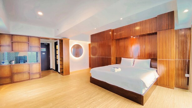 Une chambre d’hôtel moderne avec un grand lit, des lambris en bois aux murs, un luminaire circulaire et un plancher en bois.