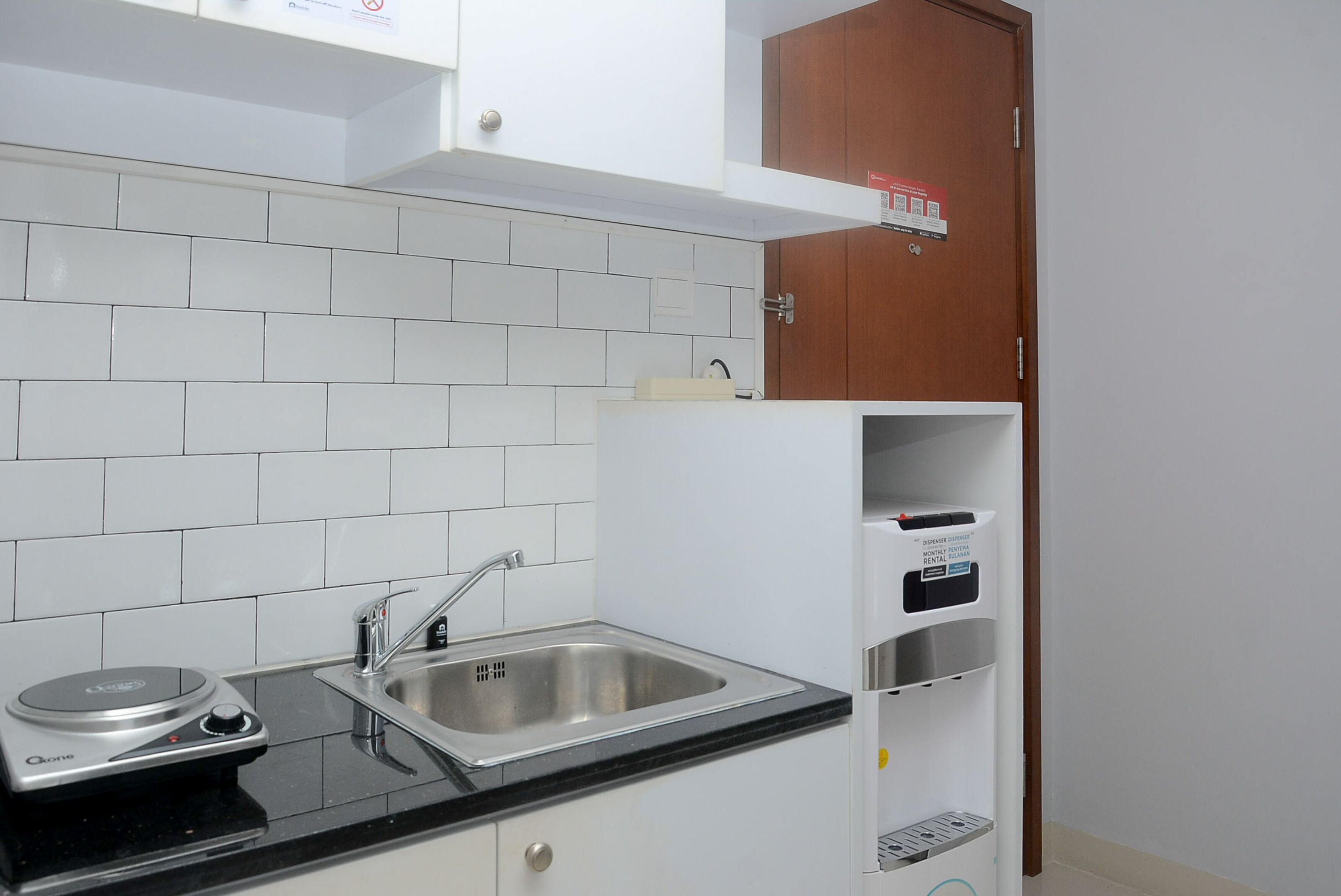 A kitchen with white tiled backsplash, a stainless steel sink, a black countertop, and a built-in oven.